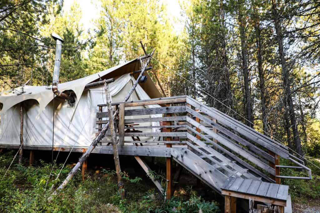 outside view of tent Under Canvas Glamping Glacier National Park with stairs and a deck, chimney and trees in the background