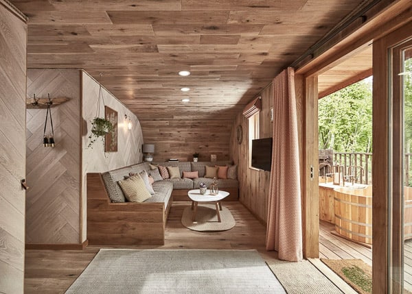 inside of a glamping cotswolds treeshouse with a view of a couch and walls, rug, sliding door to a deck with a tub