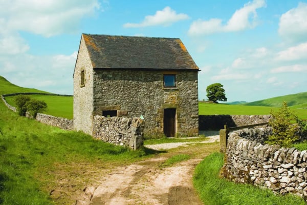 Glamping Peak District Barn with blue sky and stone fence in front of it. 