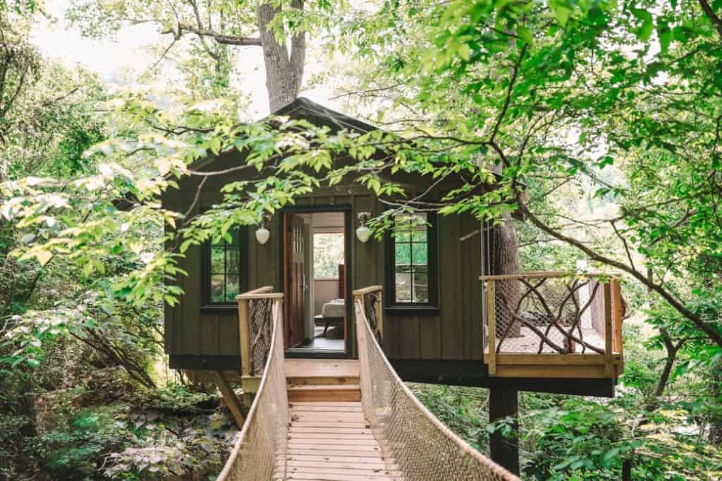 The Nest at Asheville Glamping view of the treehouse from bridge with door open and bed inside