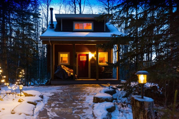 Woodsy Cabin Getaway-Four Season Paradise view of front of cabin with porch at night with lights on inside during winter