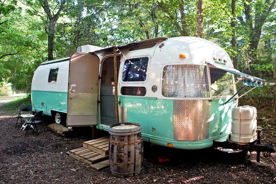 1978 Airstream Glamping - Appalachia Hemp Farm view of the side of airstream, vintage with green and white paint and a barrel table