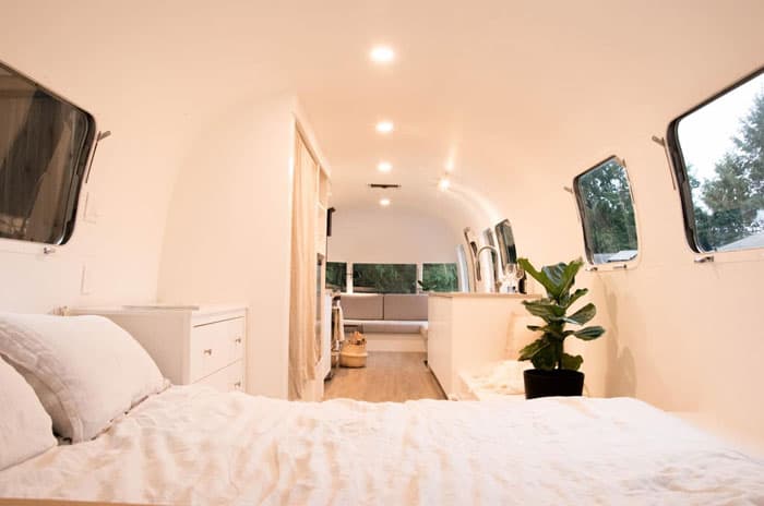 August the Airstream Salt Spring Island  view from inside the trailer with white walls, bed, plant, sink and couch in the distance