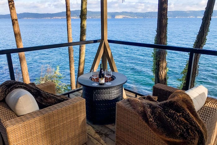 The Trincomali Hideaway Yurt view from the deck next to the water with two wicker chairs and a gas fire table with wine and glasses
